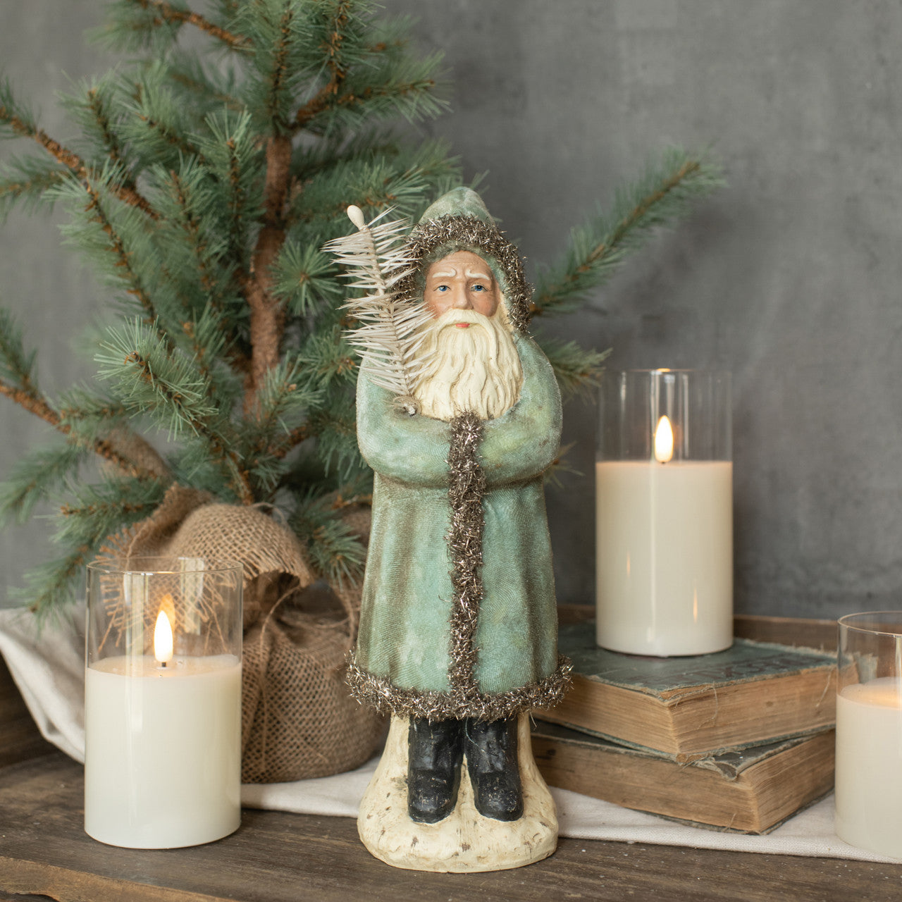 A soft blue velvet belsnickle figurine standing next to a decorative tree, with lit candles and a cozy, traditional aesthetic.