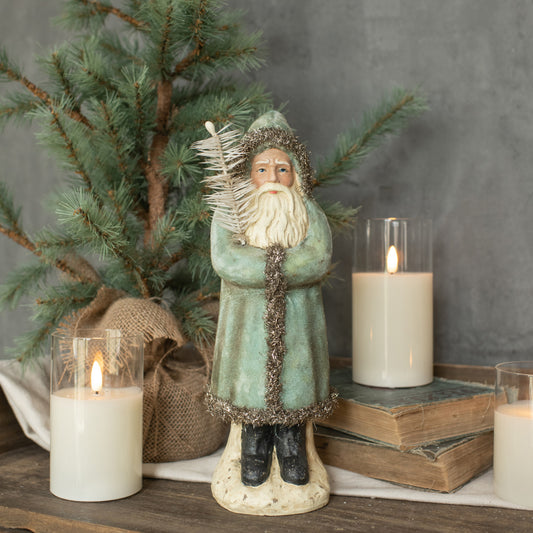 A soft blue velvet belsnickle figurine standing next to a decorative tree, with lit candles and a cozy, traditional aesthetic.