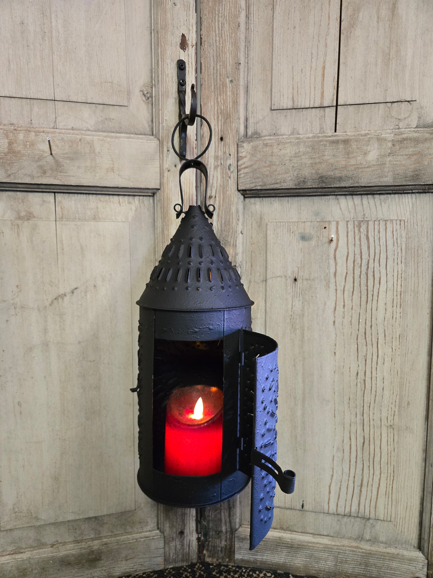 A textured black finish lantern hanging against a wooden background with a red candle inside.