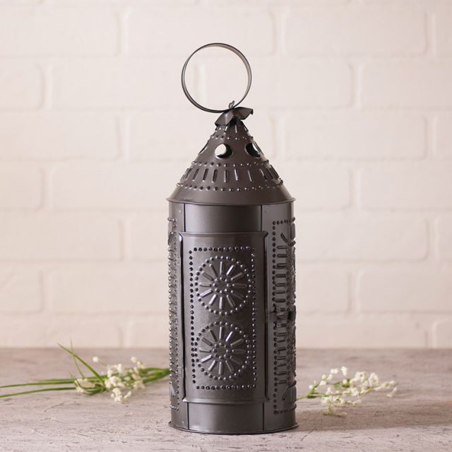 Punched tin lantern next to flowers in front of a white brick wall.