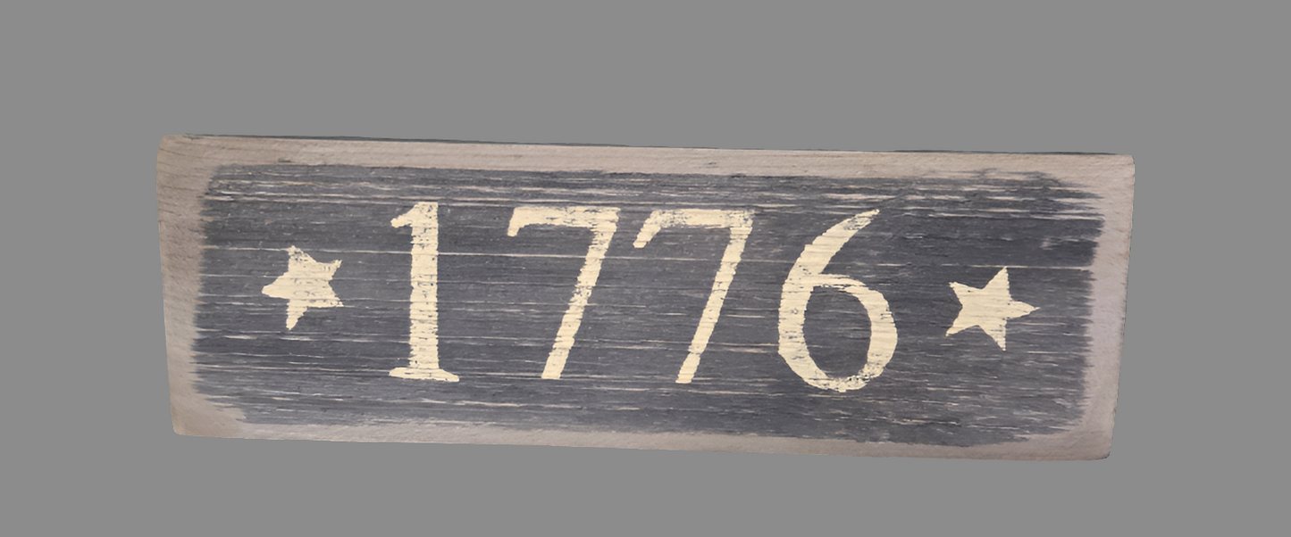 A rectangular wooden sign with the inscription '1776' in a heraldic font, surrounded by stars and asterisks on a dark background.