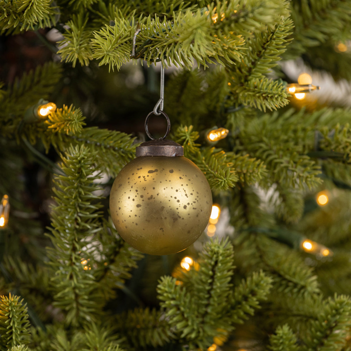 Gold ornament hanging on a Christmas tree with blurred lights in the background