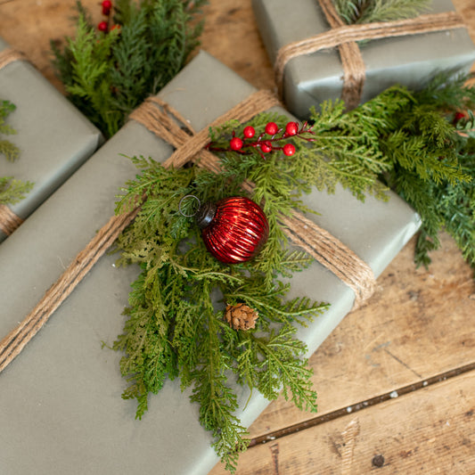 Gift wrapped in green paper with a red ornament and pine branches on a wooden surface
