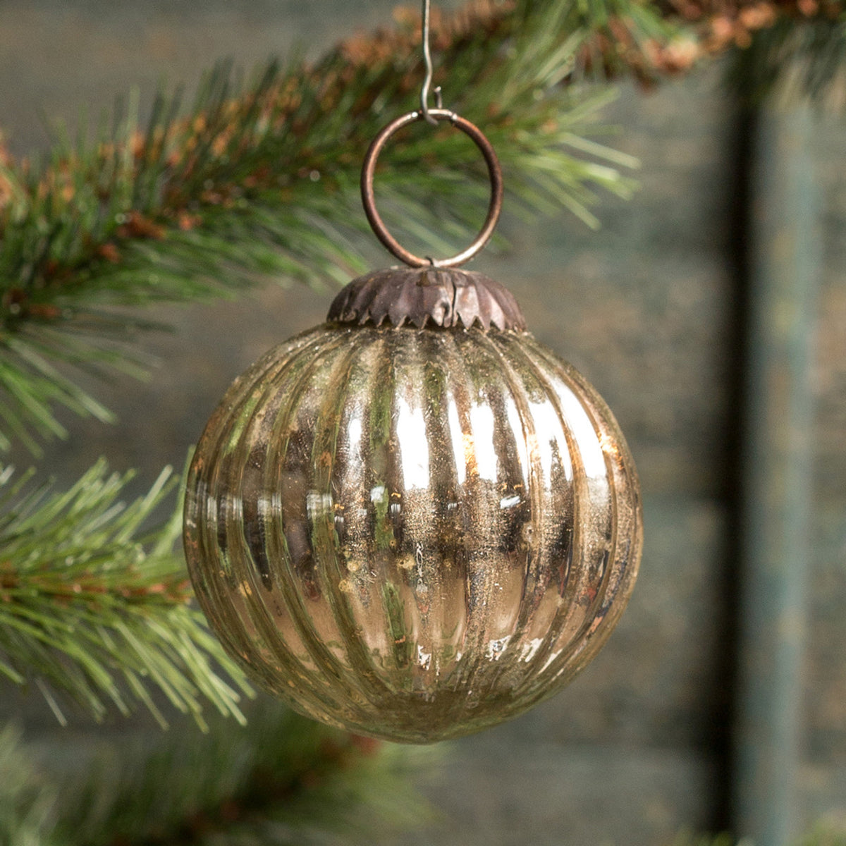 Gold ribbed glass ornament hanging on a Christmas tree branch.