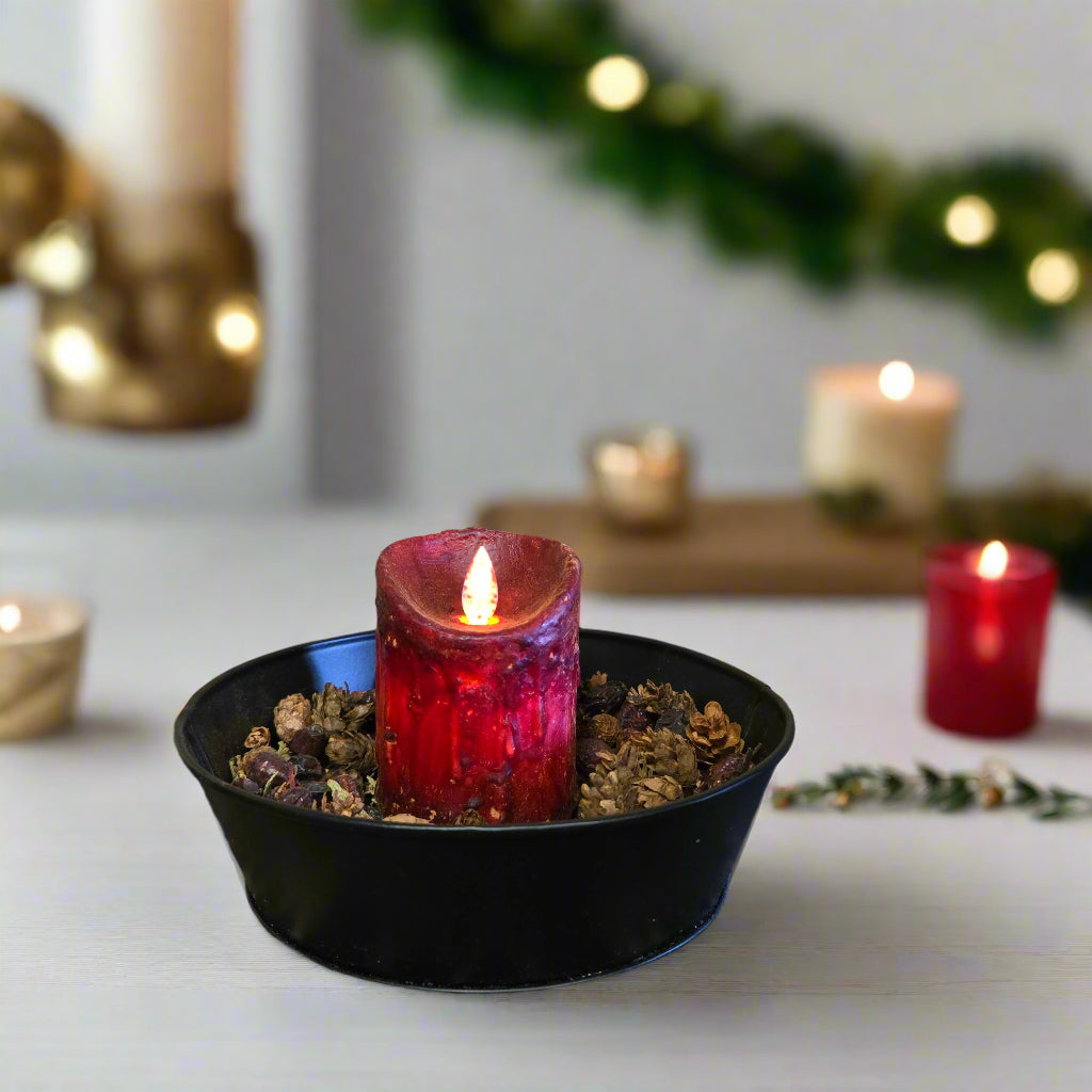 A burgundy colored LED candle with a moving flame placed in a black holder, set against a wooden background.