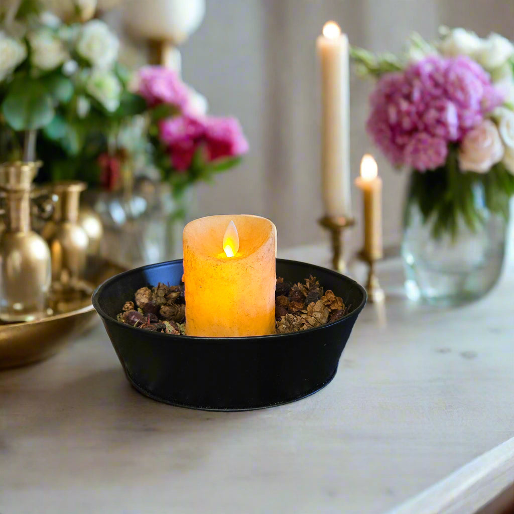 A burnt ivory colored LED candle placed in a black holder with a moving flame effect, situated on a textured surface.