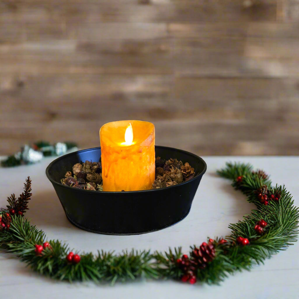 An LED candle with a moving flame effect, placed in a black holder on a textured surface, depicting a realistic flame in mustard color.
