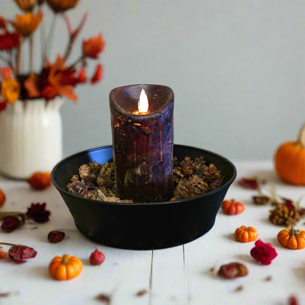 A black moving flame pillar candle appearing to glow with a warm light, placed in a black holder with a rustic design.