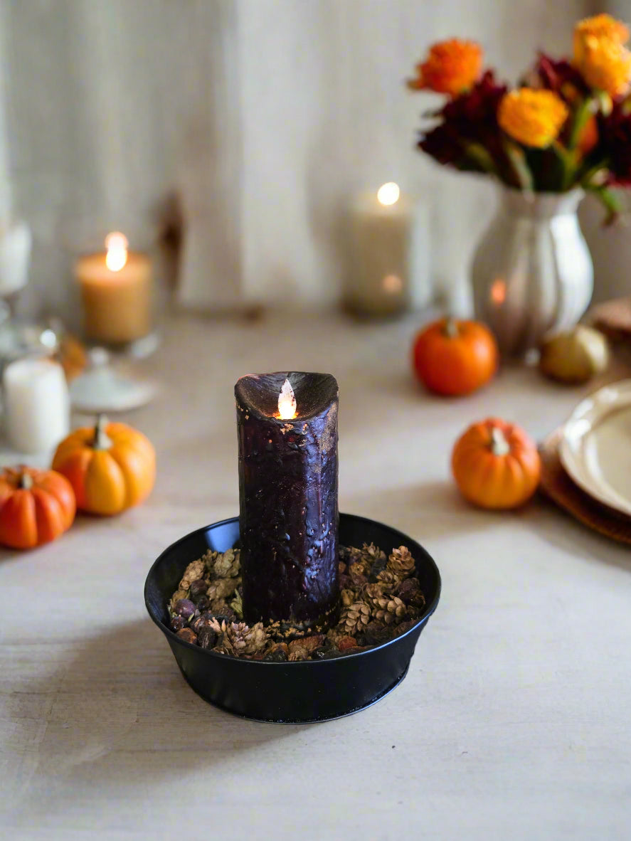A black moving flame pillar candle on a wooden surface with a patterned rug underneath.