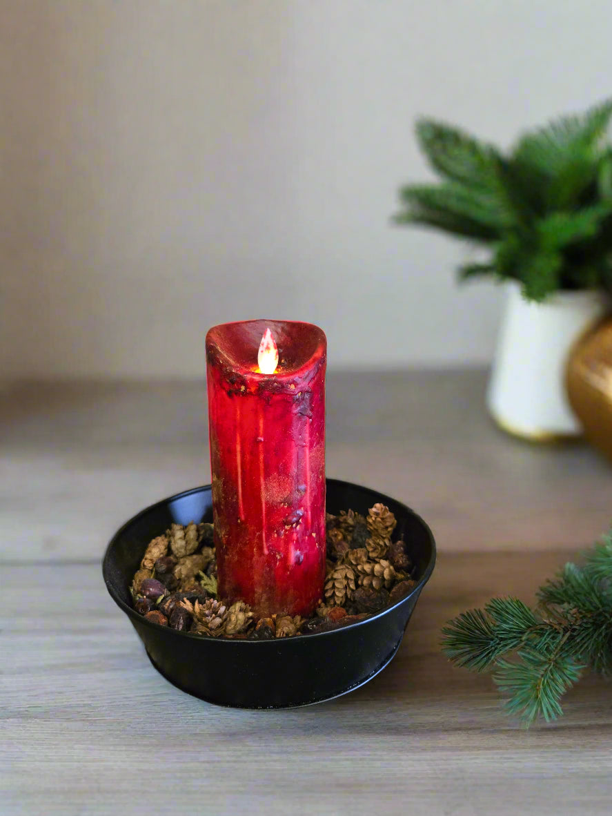 A moving flame pillar candle in a burnt burgundy color, displayed on a black surface with a rustic background.