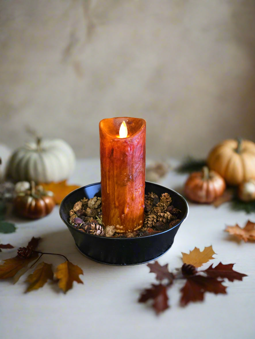 A burnt orange flameless pillar candle sitting in a black holder, designed to create a moving flame effect.