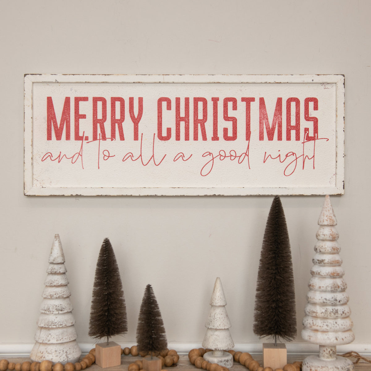 Decorative Christmas sign with 'Merry Christmas and to all a good night' text, surrounded by small Christmas trees on a neutral background.