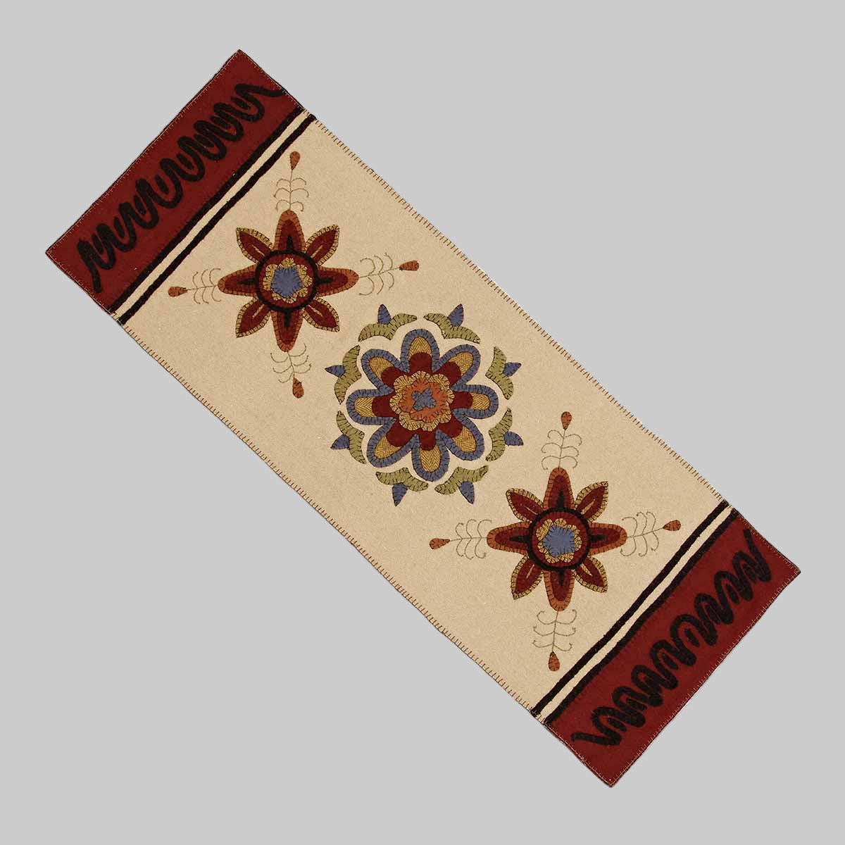 A beige cotton table runner with floral embroidery and decorative borders in brown and black colors.
