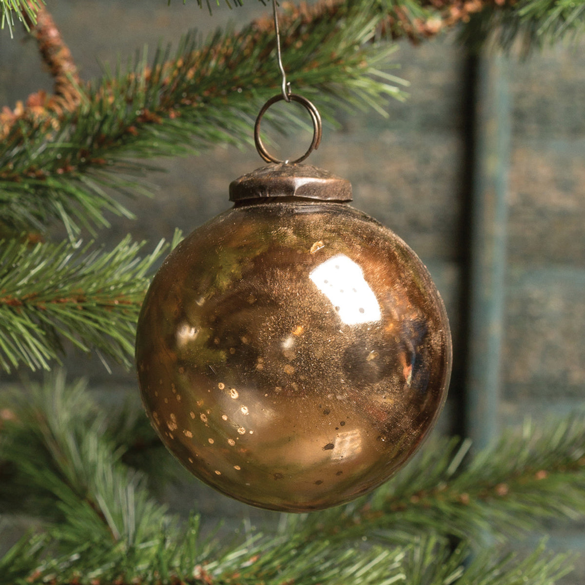 Bronze Christmas ornament hanging on a tree branch with a green background