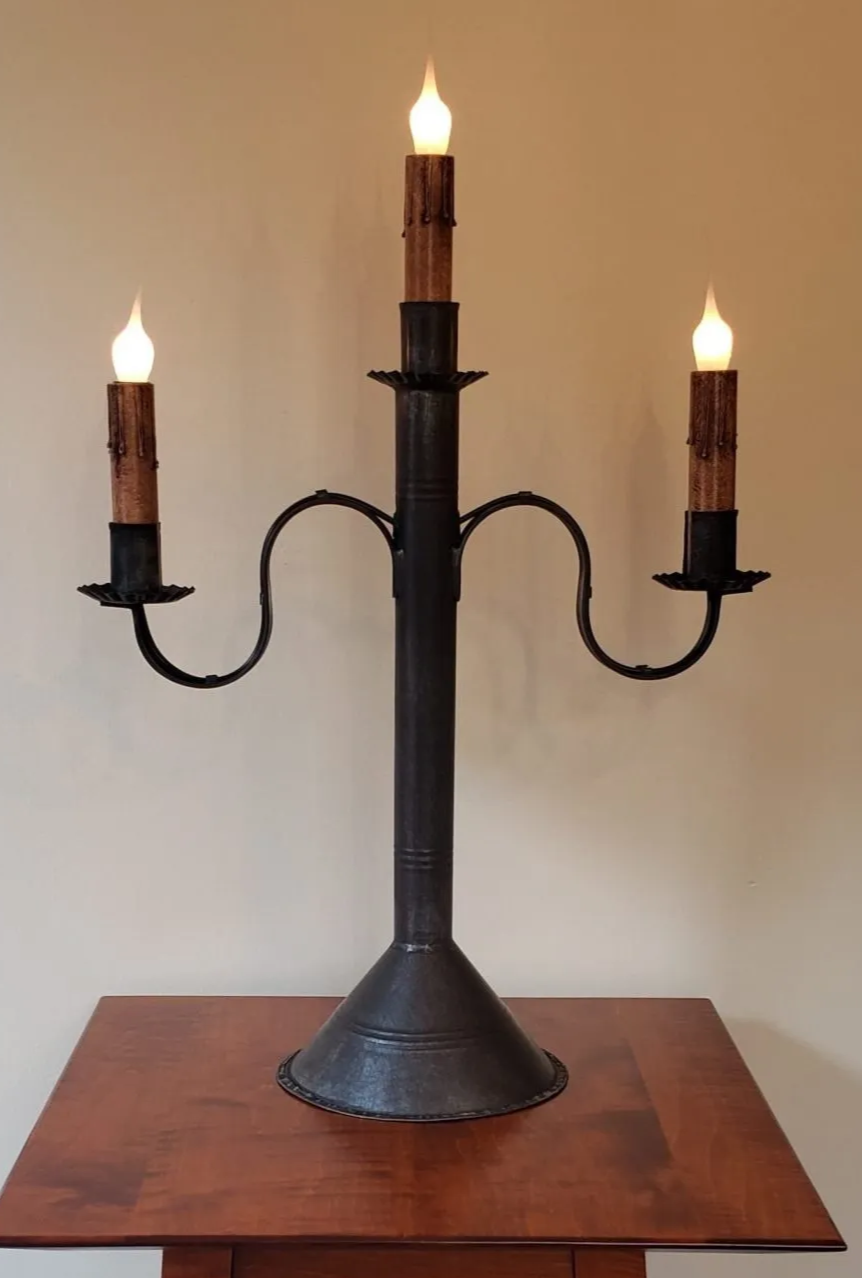 Black metal candelabra with three lit candles on a wooden surface against a plain background