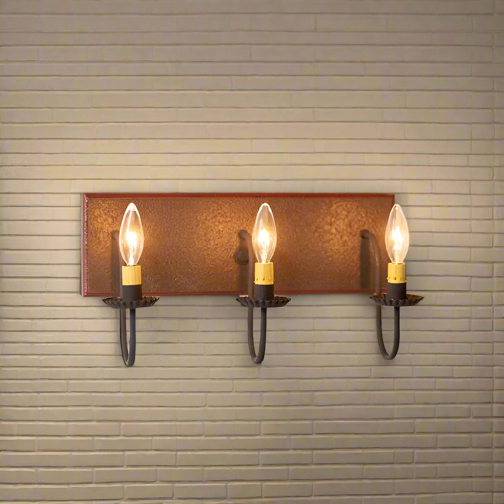 Wall-mounted light fixture with three lit candles on a white wall.