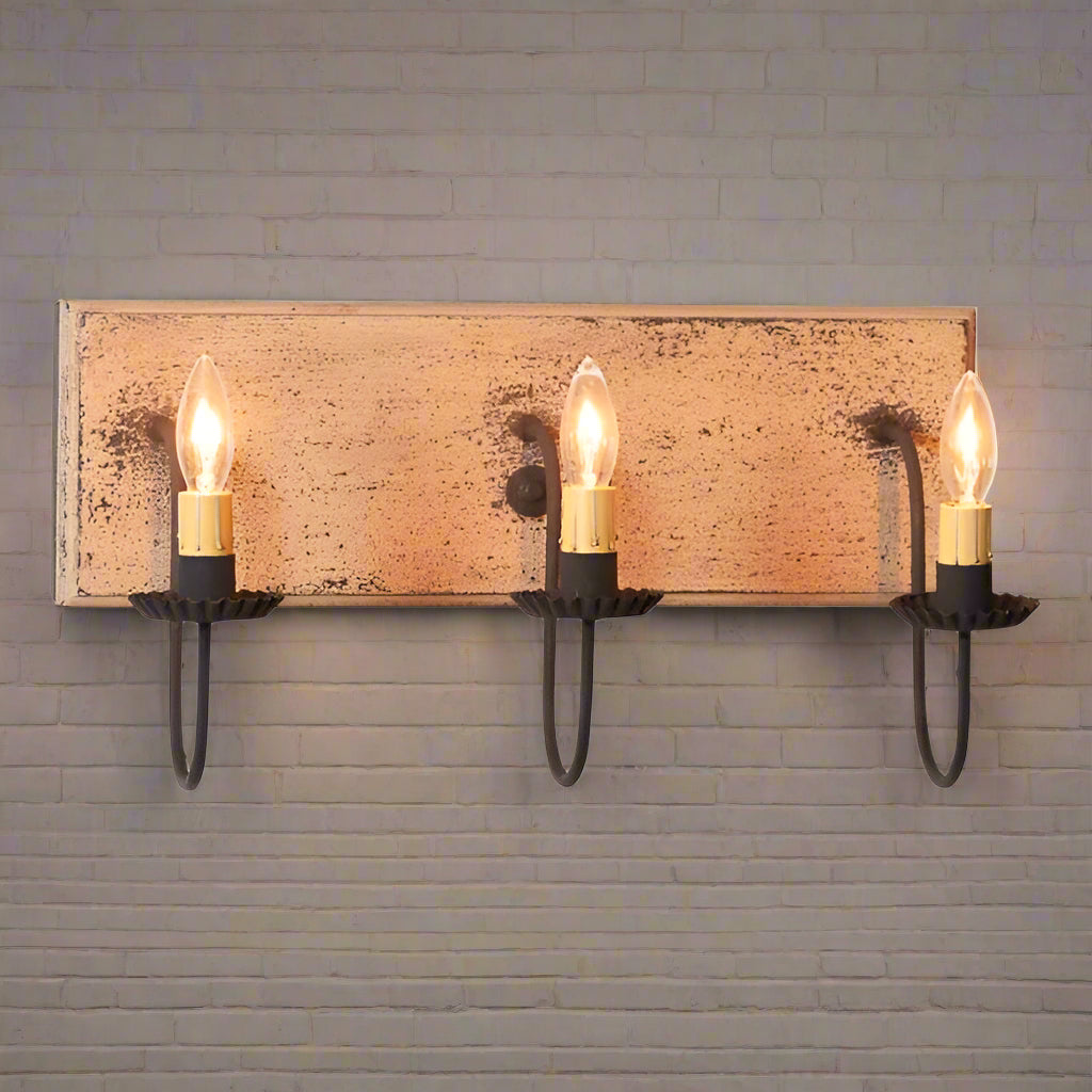 A three-light vanity light fixture with a buttermilk finish and black arms, featuring E12/Candelabra sockets.