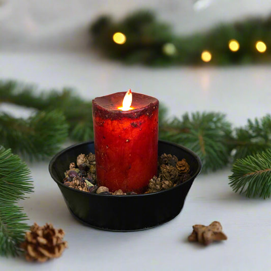 A synthetic moving flame candle in burgundy color appears to be burning, placed on a black dish on a patterned fabric.