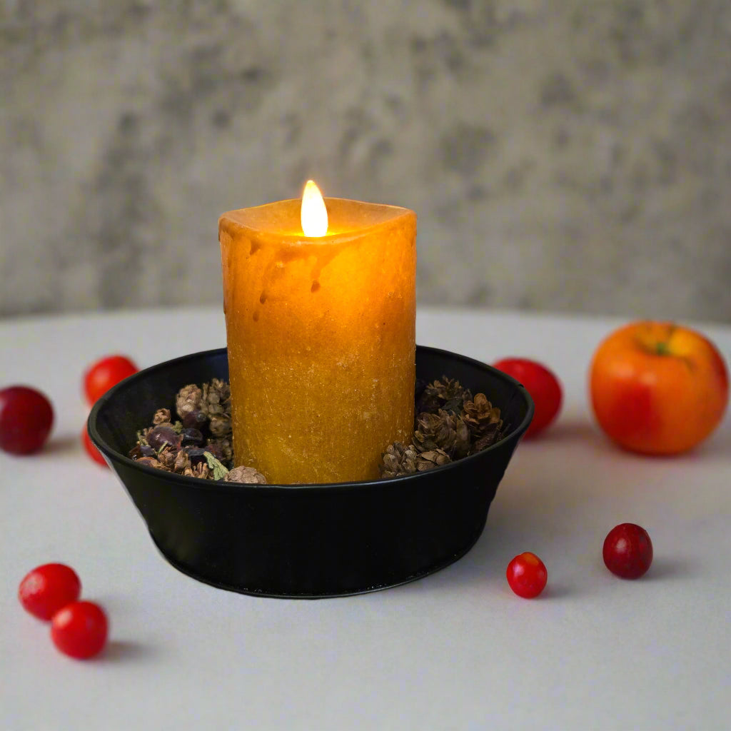 A synthetic moving flame pillar candle in mustard color displayed in a black holder with a timer feature.
