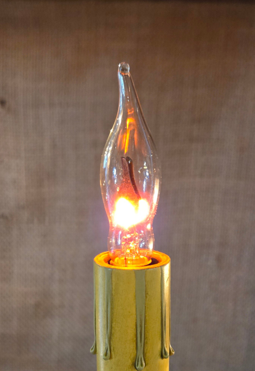 A clear incandescent bulb glowing warmly, mounted on a gold-colored base.