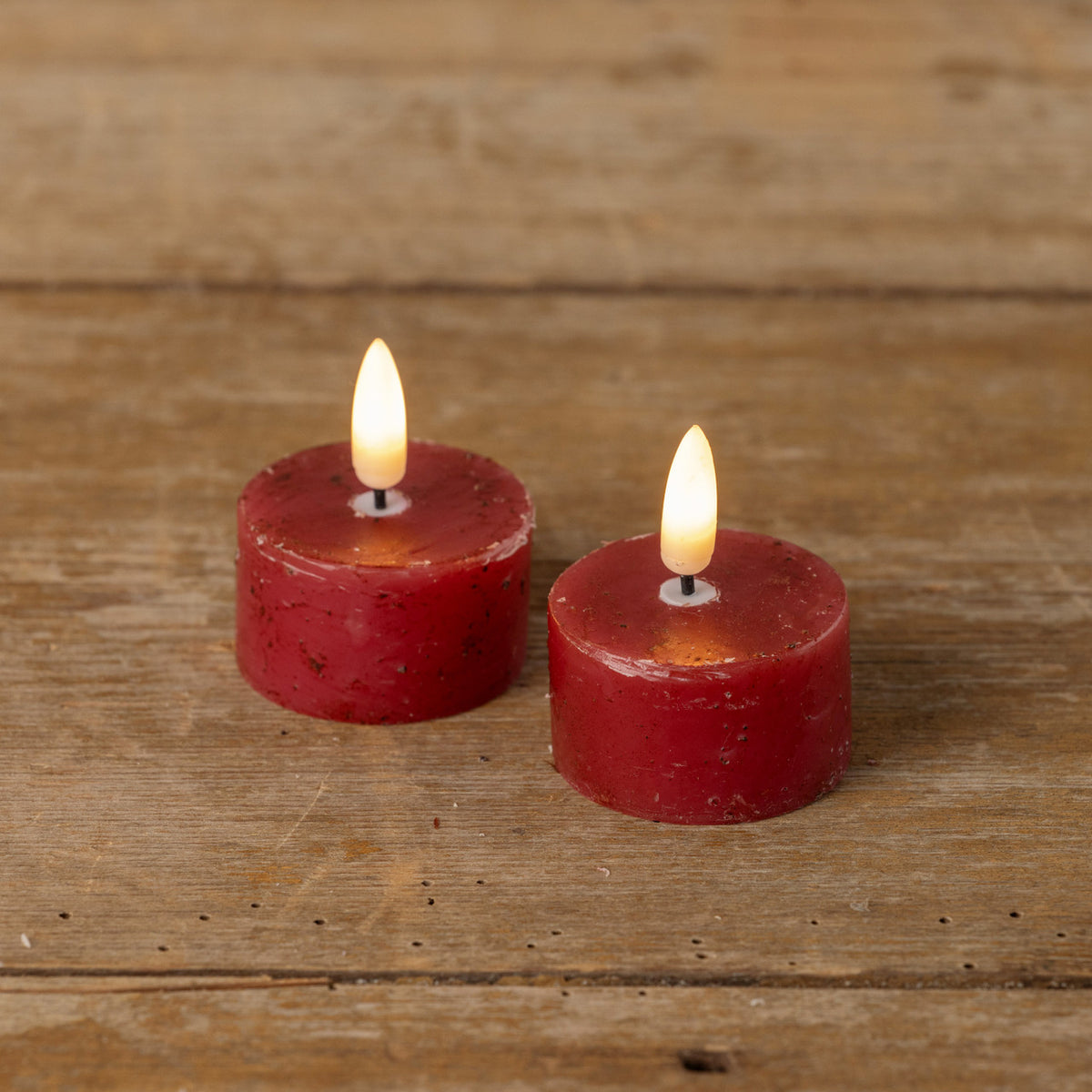 Two red candles with lit flames on a wooden surface