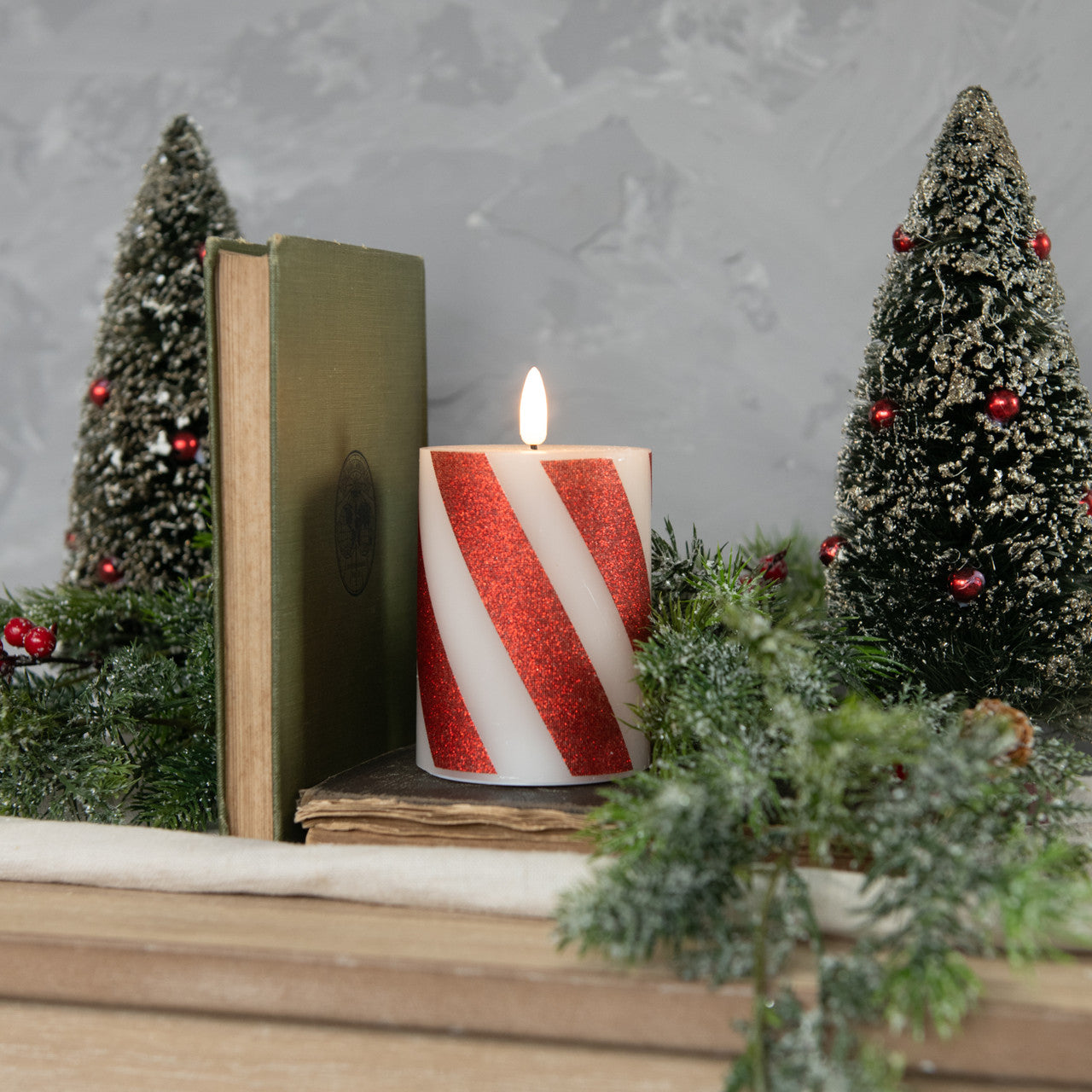 Candy cane pillar candle on mantle with bottlebrush trees, book and greenery.
