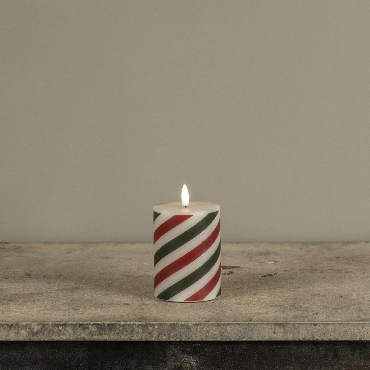 Candle with red and green stripes on a wooden surface against a gray background