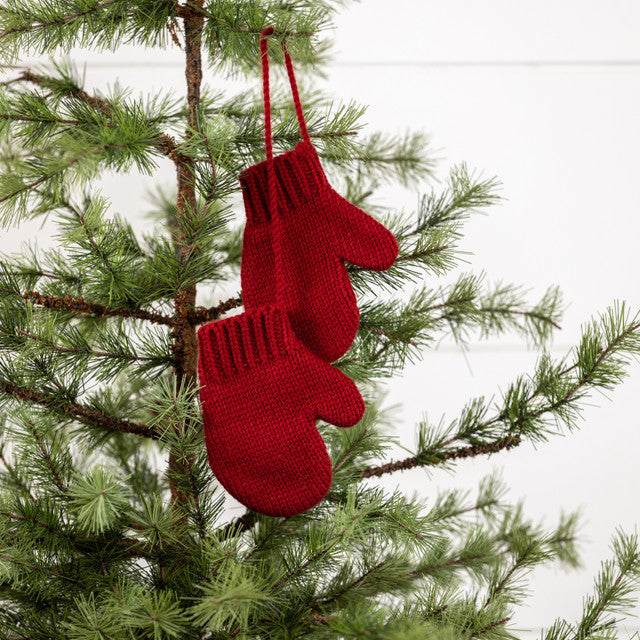 Red mitten ornaments hanging in a pine tree on a white background.