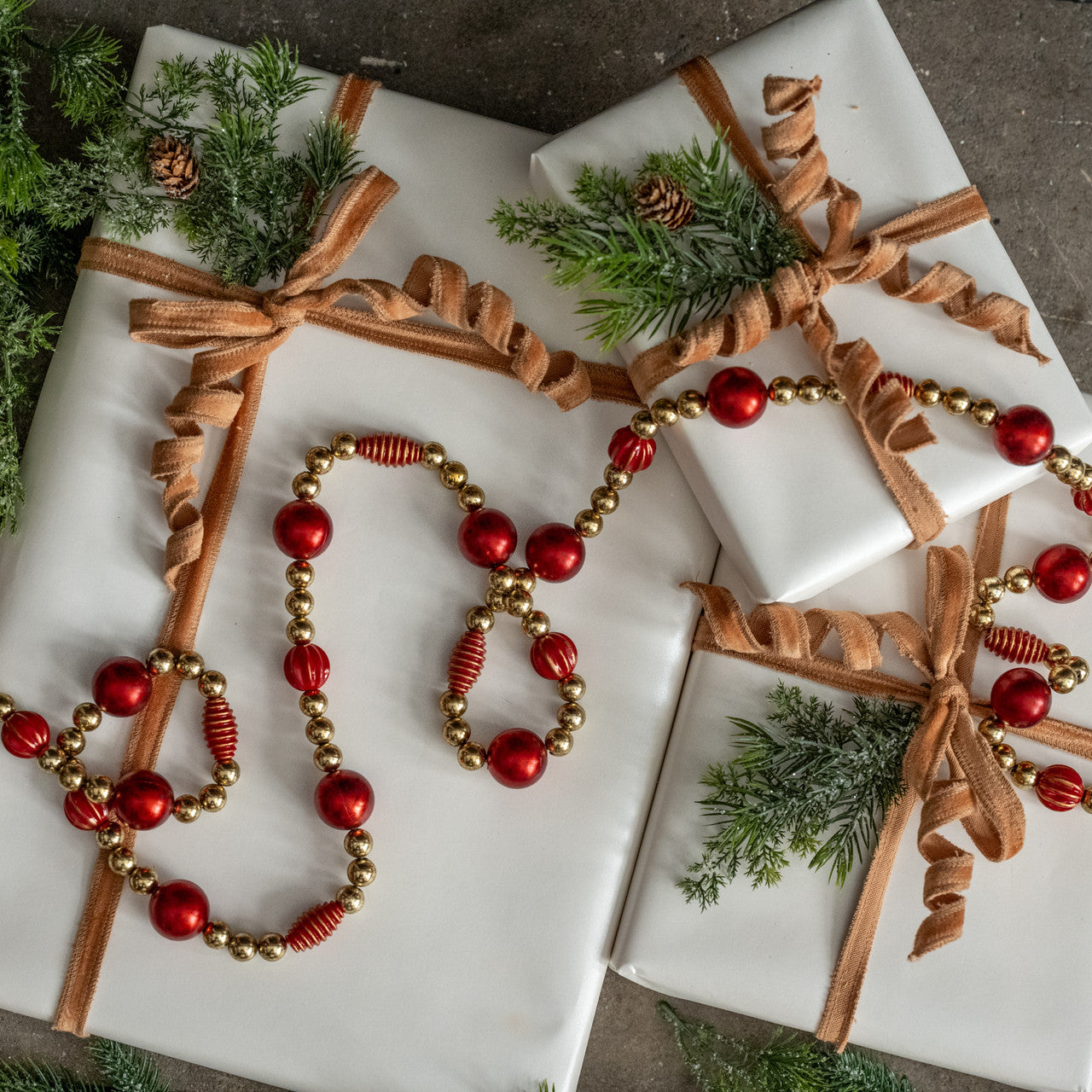 Decorative Christmas gift wrap with ribbons, beads, and greenery on a marble surface.