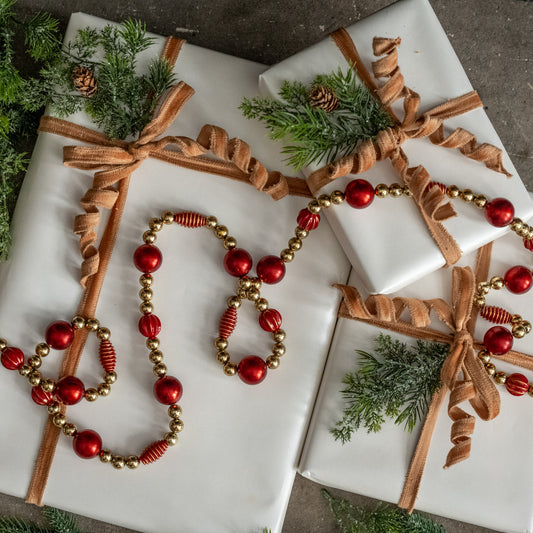 Decorative Christmas gift wrap with ribbons, beads, and greenery on a marble surface.