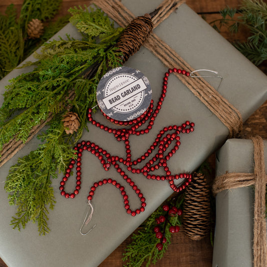 A spool of red bead garland placed on a green gift wrap, with holiday decorations around it.