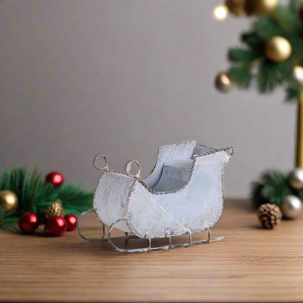 A 7-inch rustic white wash tin sleigh with solid steel runners, placed on a white surface against a background of plain walls.
