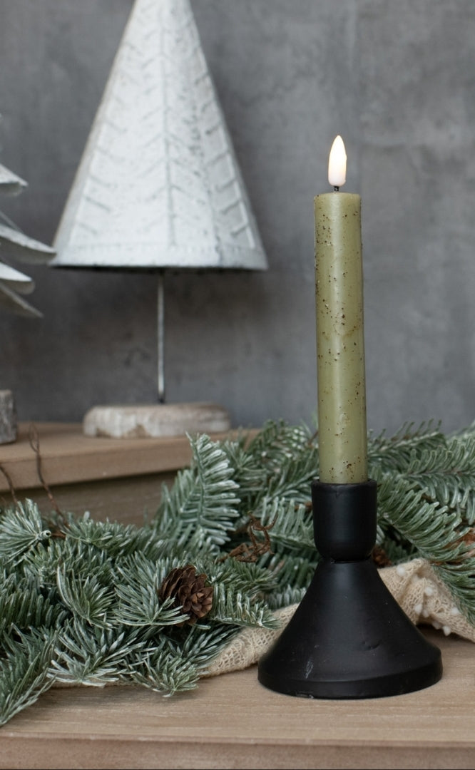 Candle in a black holder with greenery and a decorative tree in the background