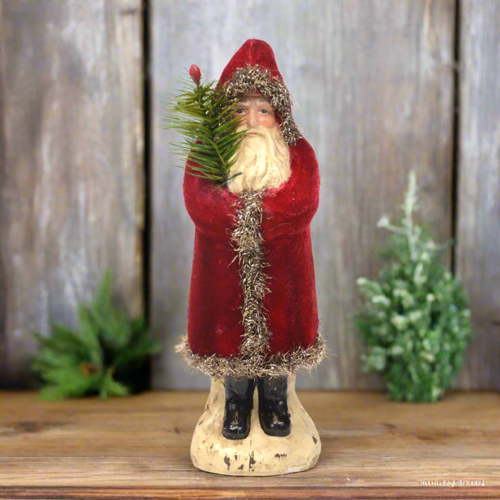Decorative figure of Santa Claus holding a Christmas tree with greenery in the background