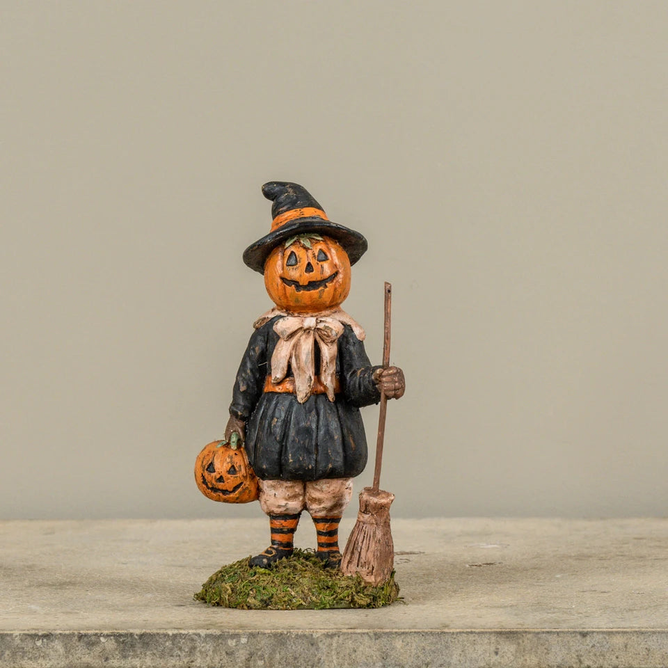 Pumpkin figurine dressed as a witch holding a broom and pumpkin on a wooden surface.