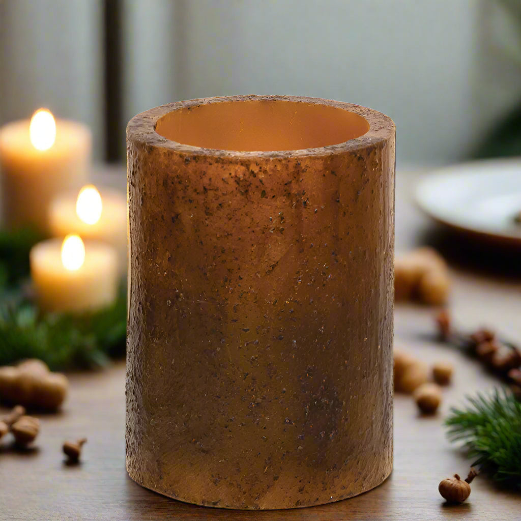A cylindrical burnt mustard colored candle pillar with a textured wax coating.
