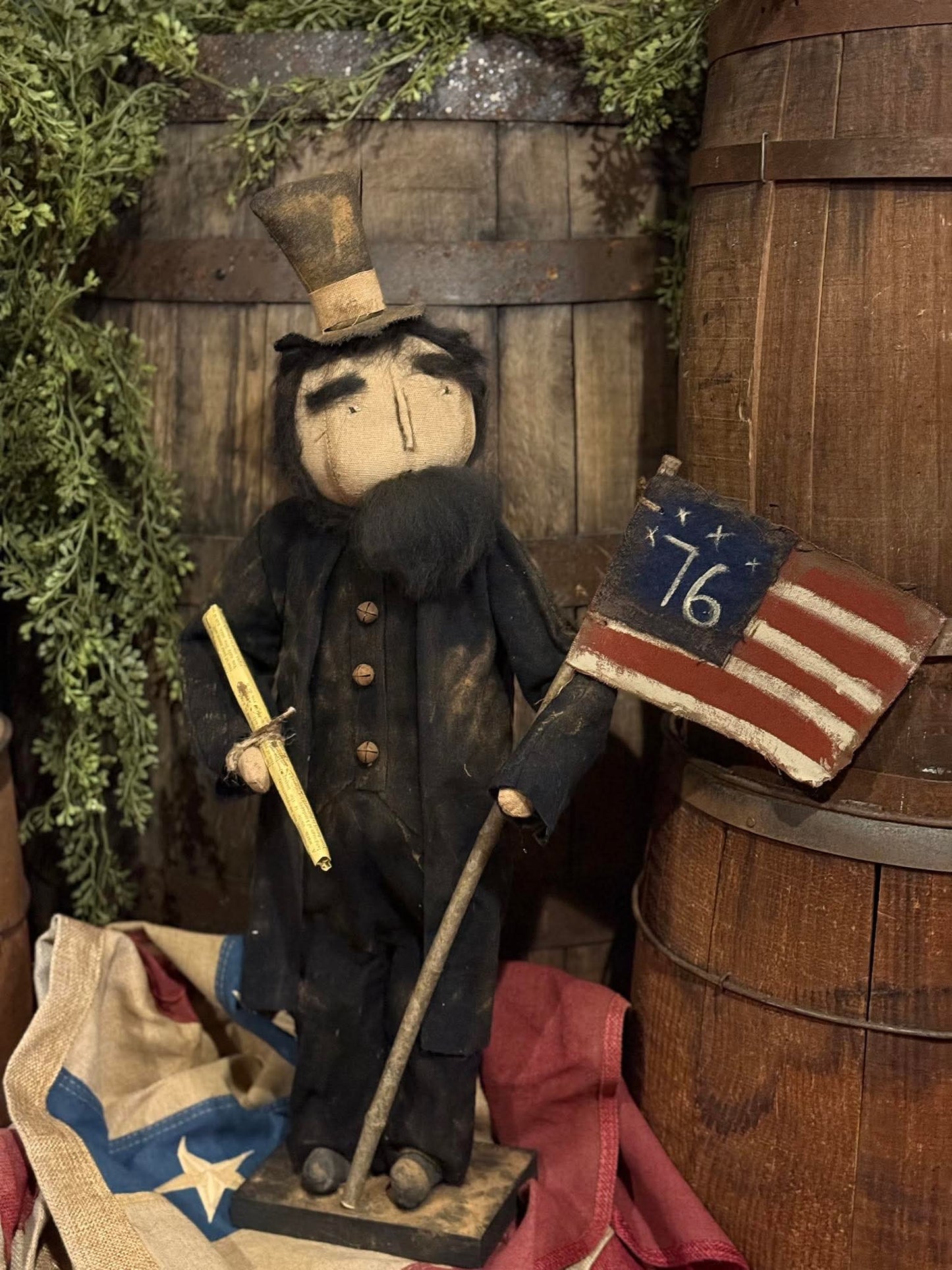 Vintage-style doll with top hat, sword, and American flag in a rustic setting
