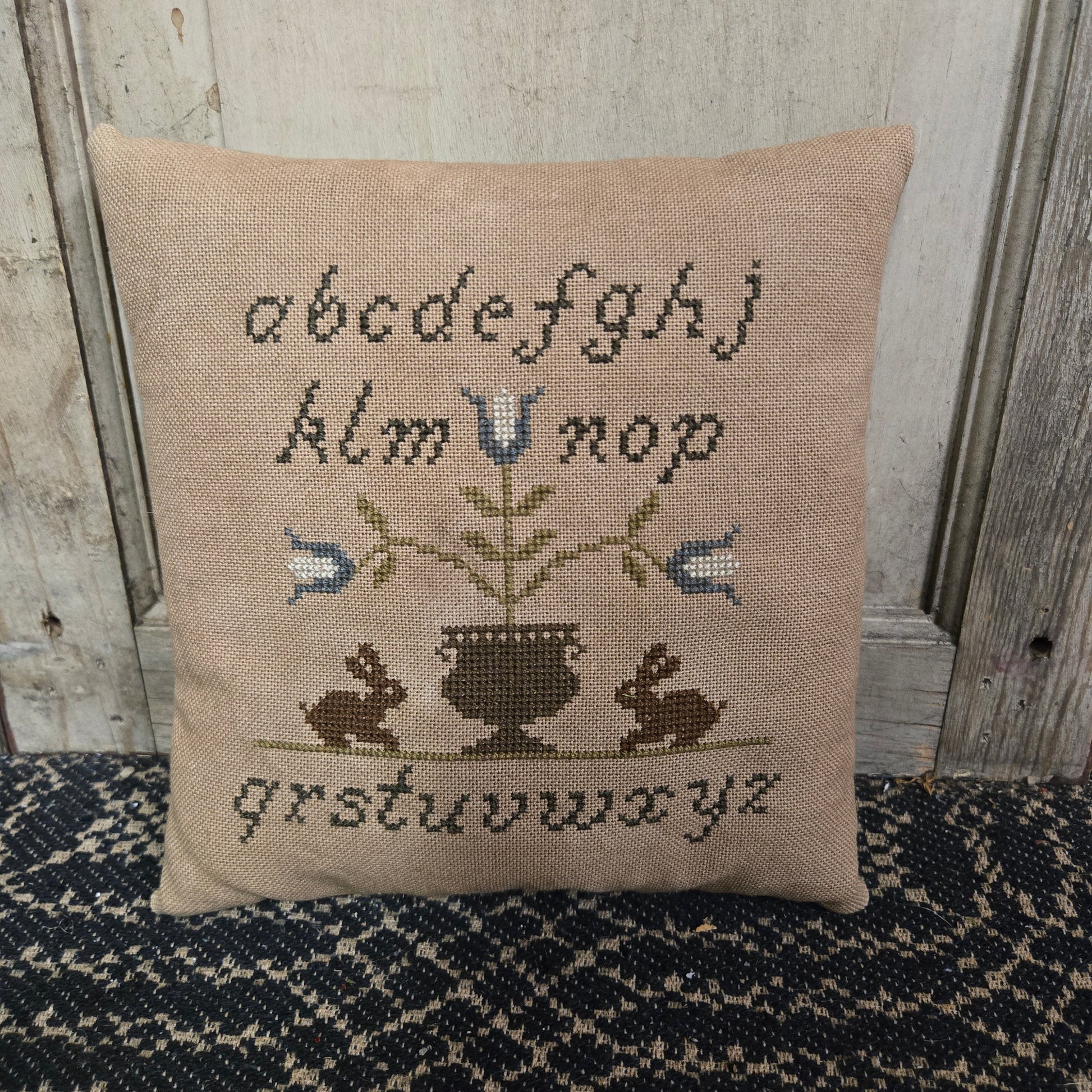 Cross stitch pillow with the alphabet and a pot of flowers