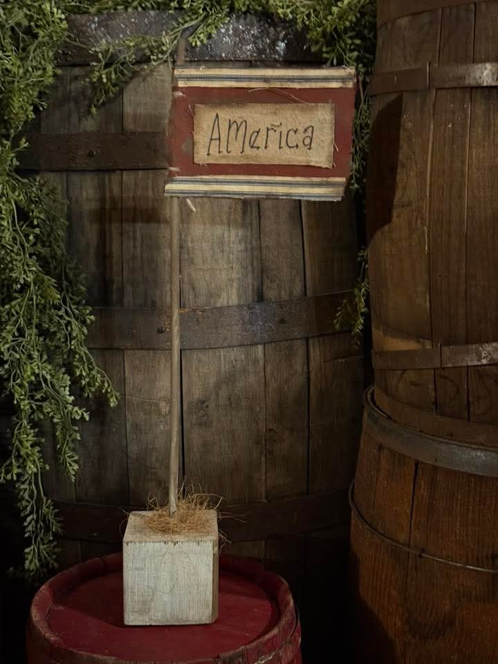 Decorative sign with 'America' on a wooden stand against a rustic wooden wall.