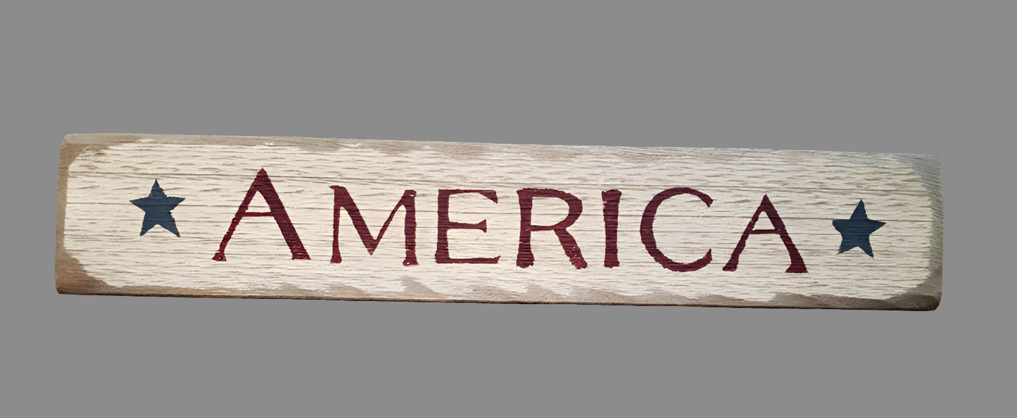 A wooden sign with the word 'America' printed in bold red letters, surrounded by star graphics, on a wooden surface.