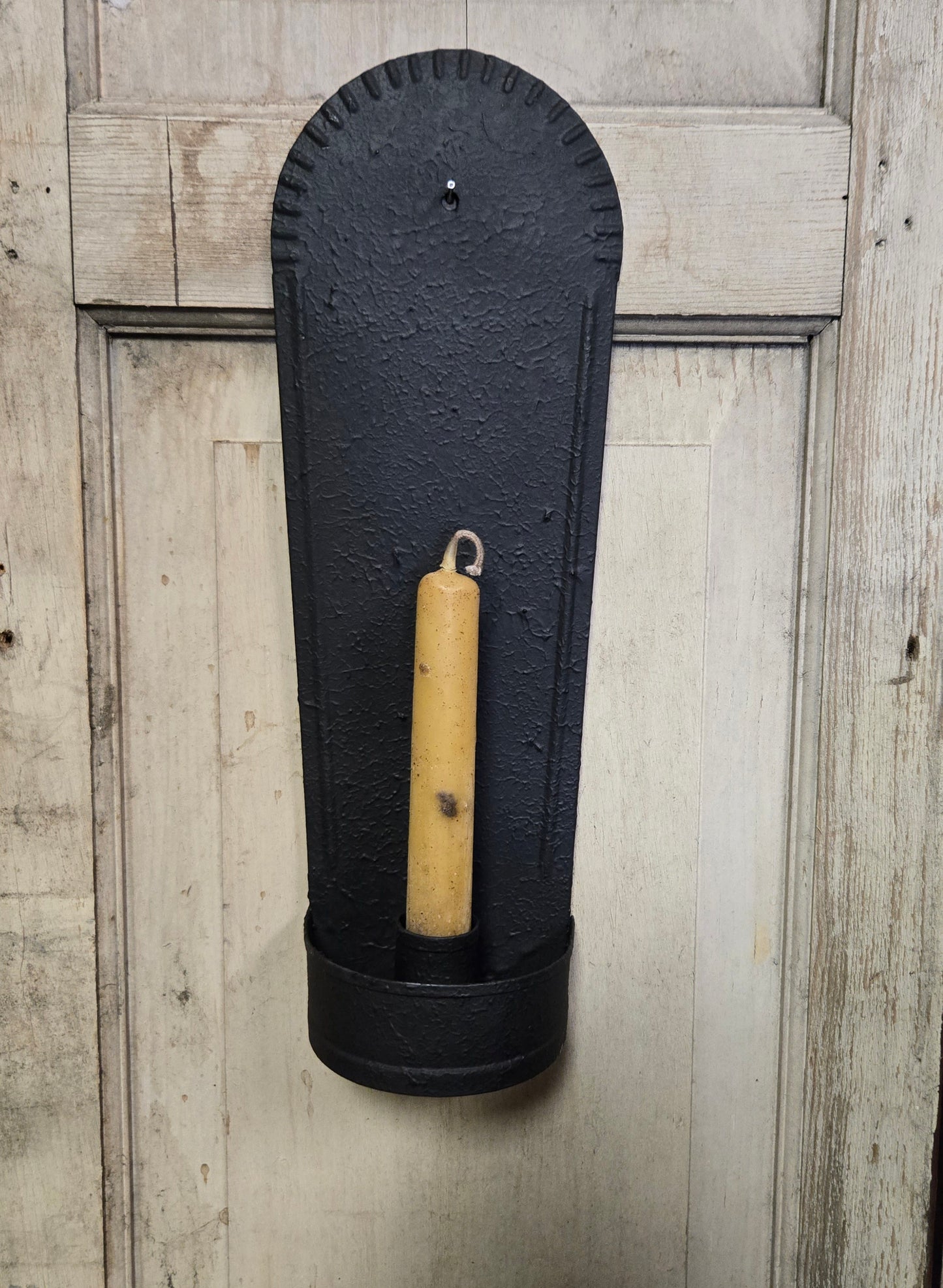 Black wall-mounted candle holder with a beige candle against a wooden background