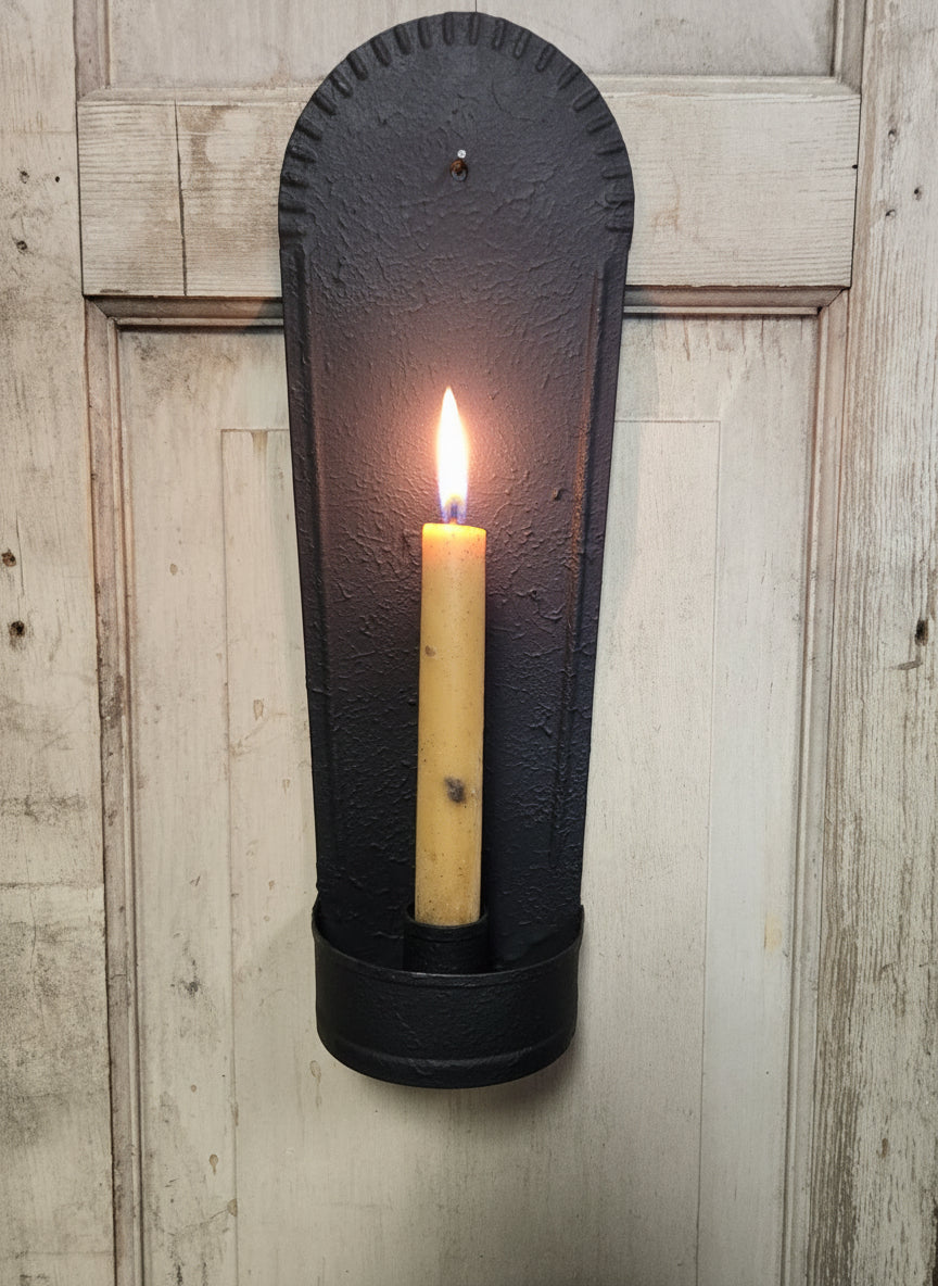 Black wall-mounted candle holder with a beige candle against a wooden background