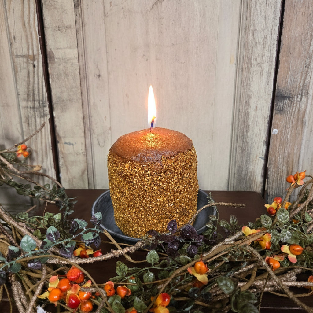 Decorative wreath with berries and a textured brown candle against a wooden background