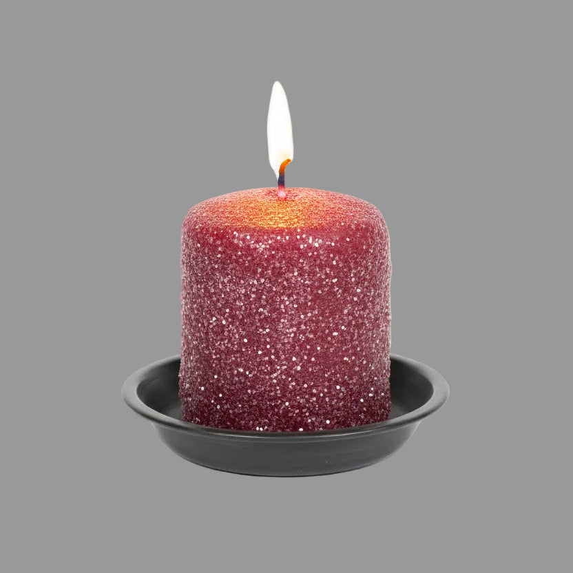 Red candle with glitter in a tin container on a wooden surface