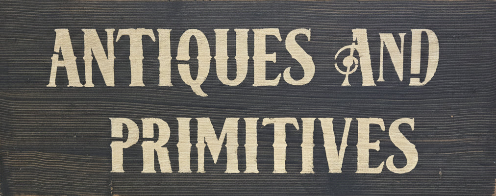 Wood sign hand painted with the words 'ANTIQUES AND PRIMITIVES'