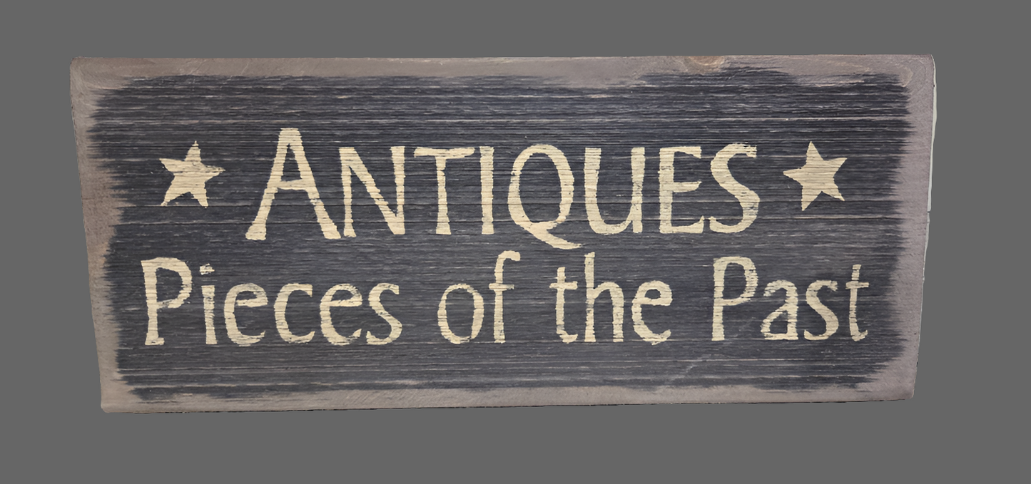 A wooden sign with the text 'ANTIQUES PIECES OF THE PAST' distressed in a rustic style.