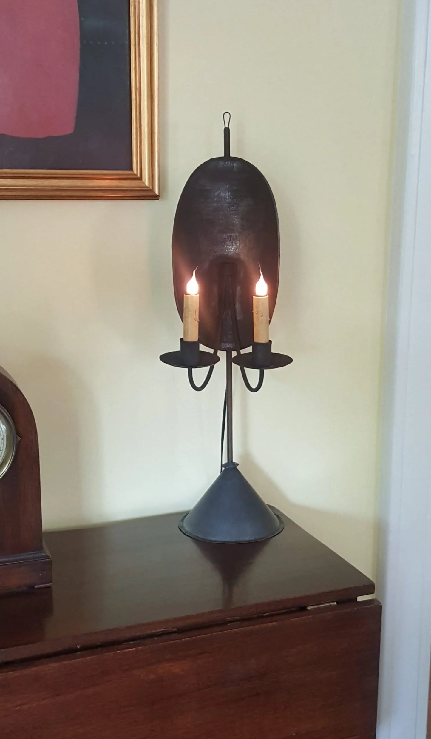 A rustic black Auburn Tin Table Light with a lantern-shaped top holding two candles, mounted on a wooden surface.