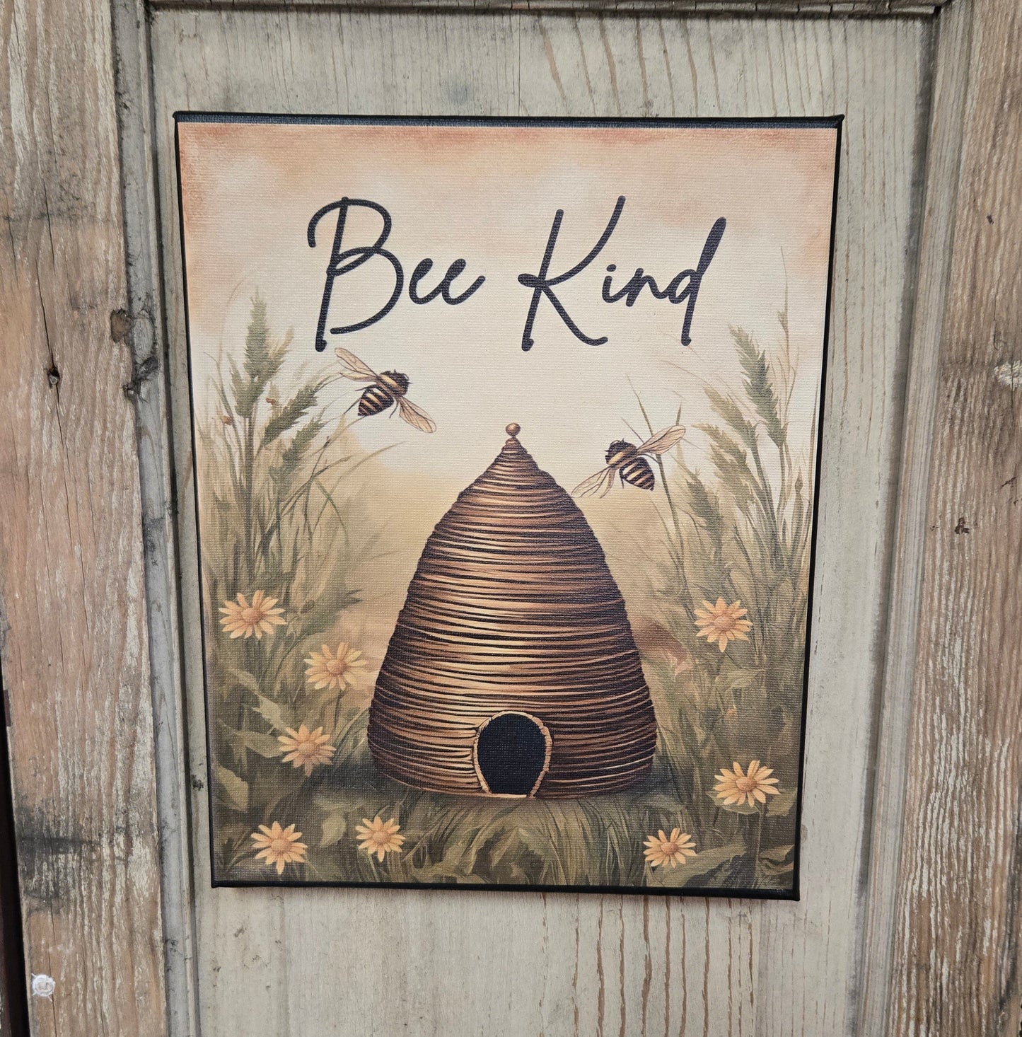 A canvas print with a bee hive and the text 'Bee Kind' displayed on it, mounted on a wooden door.