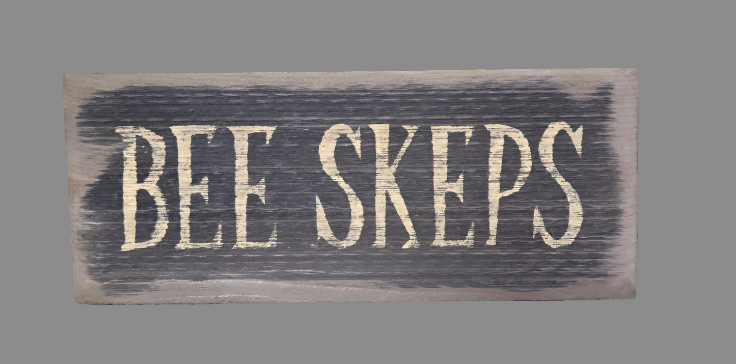 A wooden sign with the words 'BEE SKEPS' written in black.