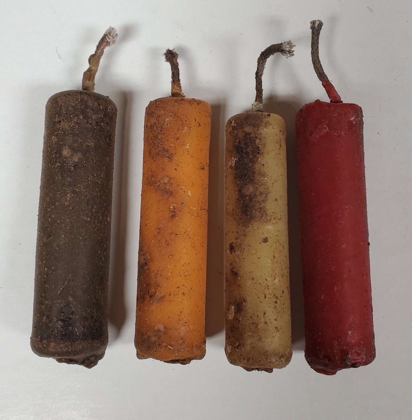 A set of four beeswax tapers in different colors including brown, orange, beige, and red, arranged side by side.